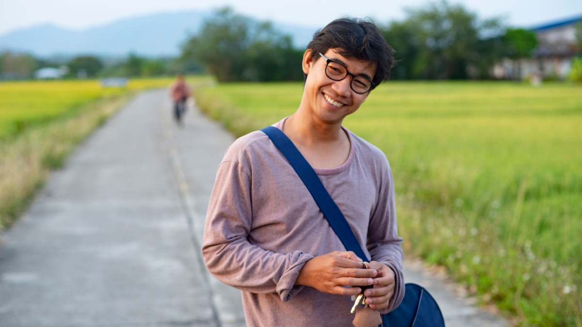 Portrait of an Asian Thai man looking humble and relaxed surrounded by rice field and in the background there is an unknown person riding a bicycle.