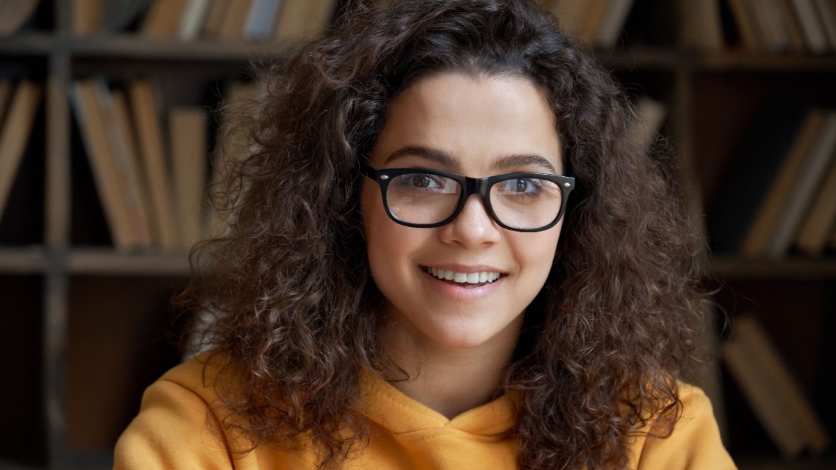 Happy hispanic woman wear glasses posing in library classroom.
