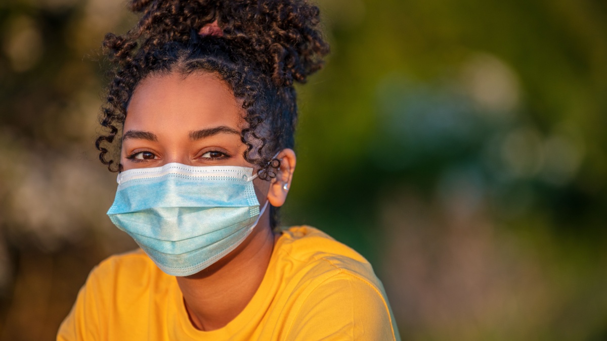 Mixed race African American teenager teen girl young woman wearing a face mask outside during the Coronavirus COVID-19 virus pandemic.