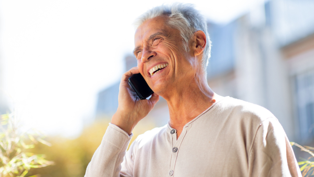 Close up portrait happy older man talking with mobile phone outside.