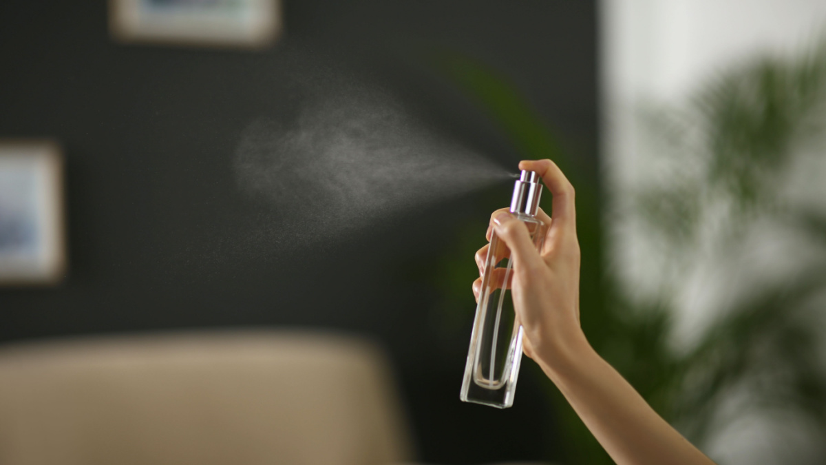 Woman spraying air freshener at home, closeup. Space for text