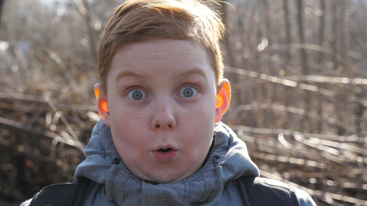 Portrait of ginger child with freckles showing surprise and amazement outdoor. Little red-haired boy looking into camera with wow expression.