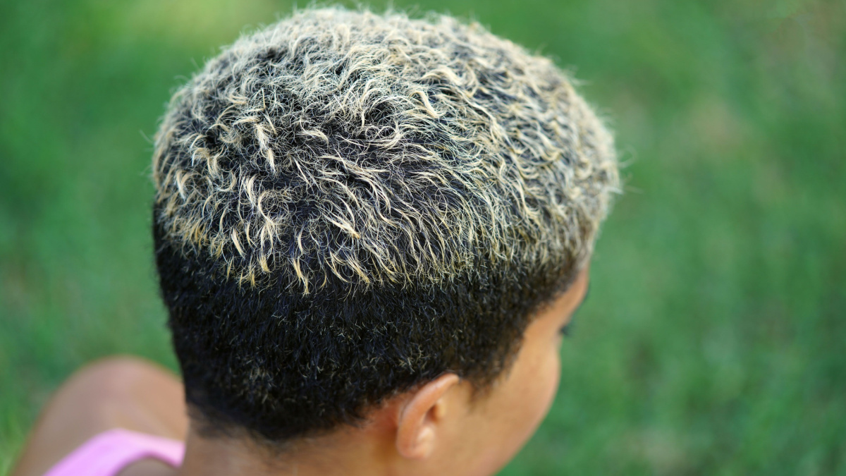 Beautiful young multicultural woman shows off her short hairstyle with two tones and white tips while sitting on the grass at the park on a sunny, warm day