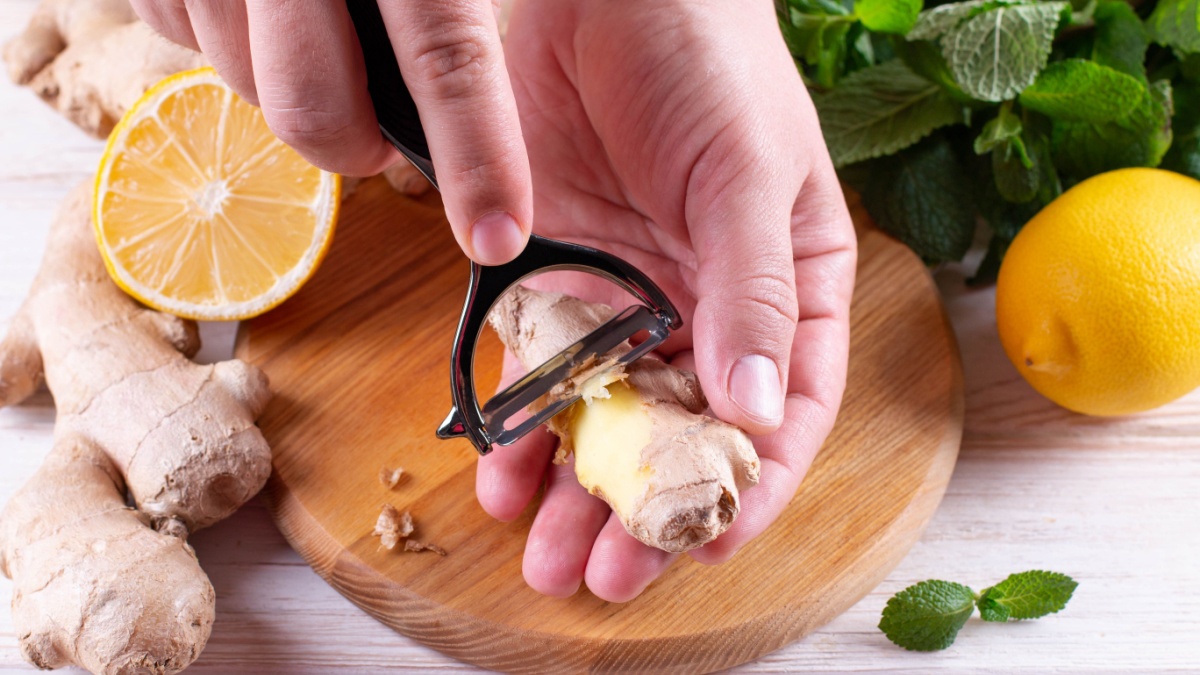 Man hands peeling fresh ginger root with knife on wood board