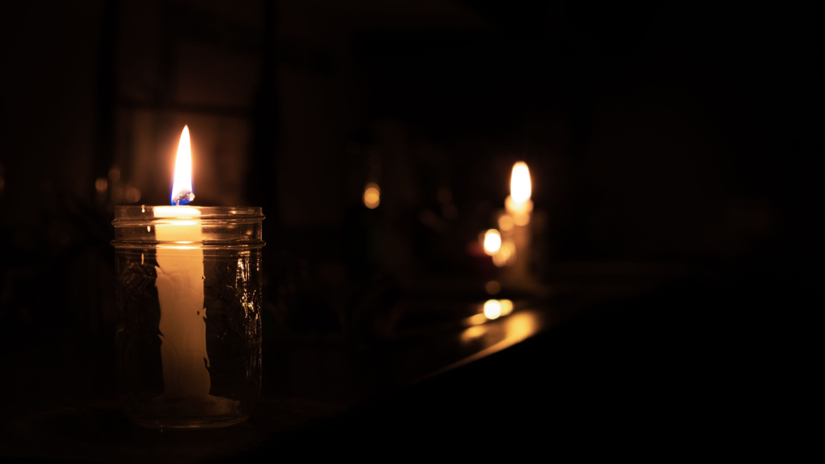 Candles on kitchen counter during power outage. 2 candles are inside a mason jar. Pitch black room except the candle lights. Selective focus on first candle with bokeh lights in the back.
