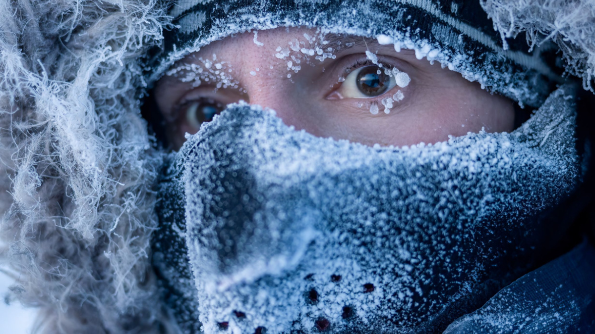 Portrait of a man in winter clothes and a mask. A traveler in the Arctic. Ice and snow on eyelashes, face and mask. Cold polar climate. Extreme travel and expeditions to the far North to the Arctic.