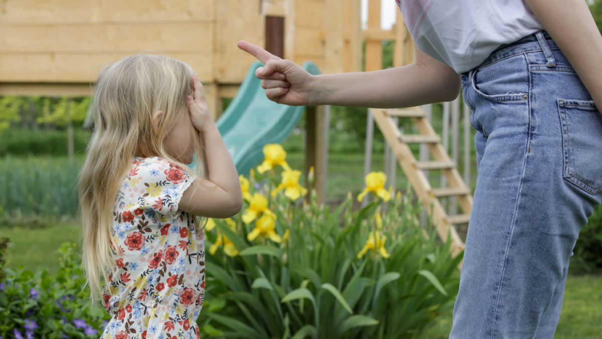 Mother is shouting at her daughter in public park. Upset little girl is crying in front of her mother.
