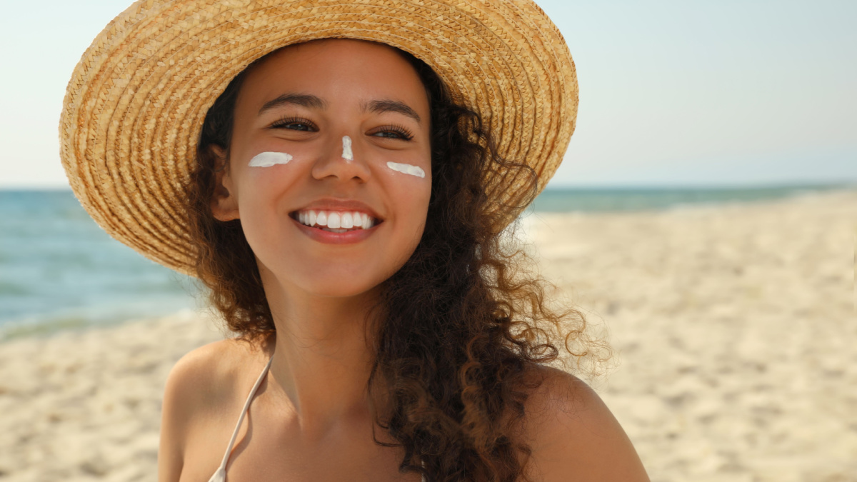 Beautiful African American woman with sun protection cream on face at beach.