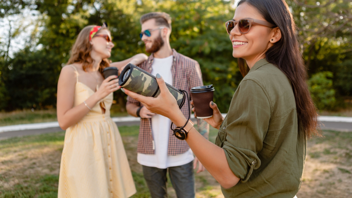 young hipster company of friends having fun together in park smiling listening to music on wireless speaker, summer style season