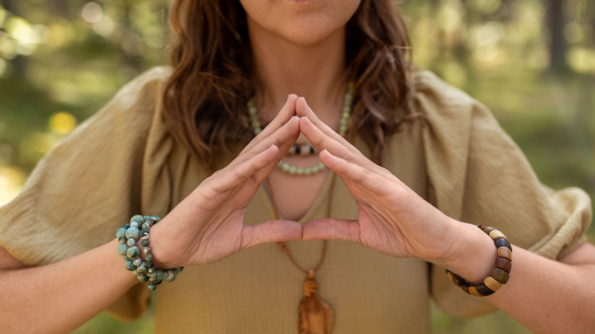 magic, spirituality and supernatural concept - close up of woman or witch making triangle of power gesture in forest.