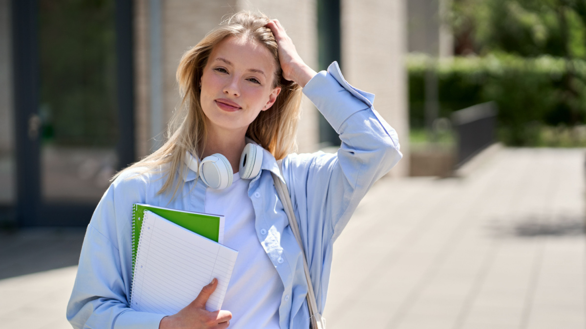 Pretty smiling girl university student holding notebooks looking at camera posing for outdoor portrait.