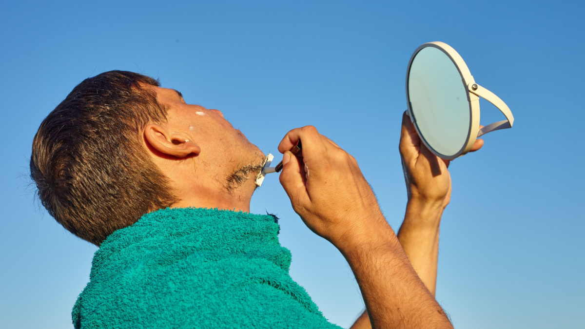 A man shaves. Shaving outside at dawn . Shave in the rays of the rising summer sun.