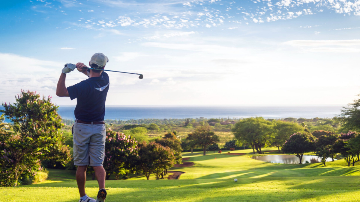 Man hitting golf ball down hill towards ocean and horizon