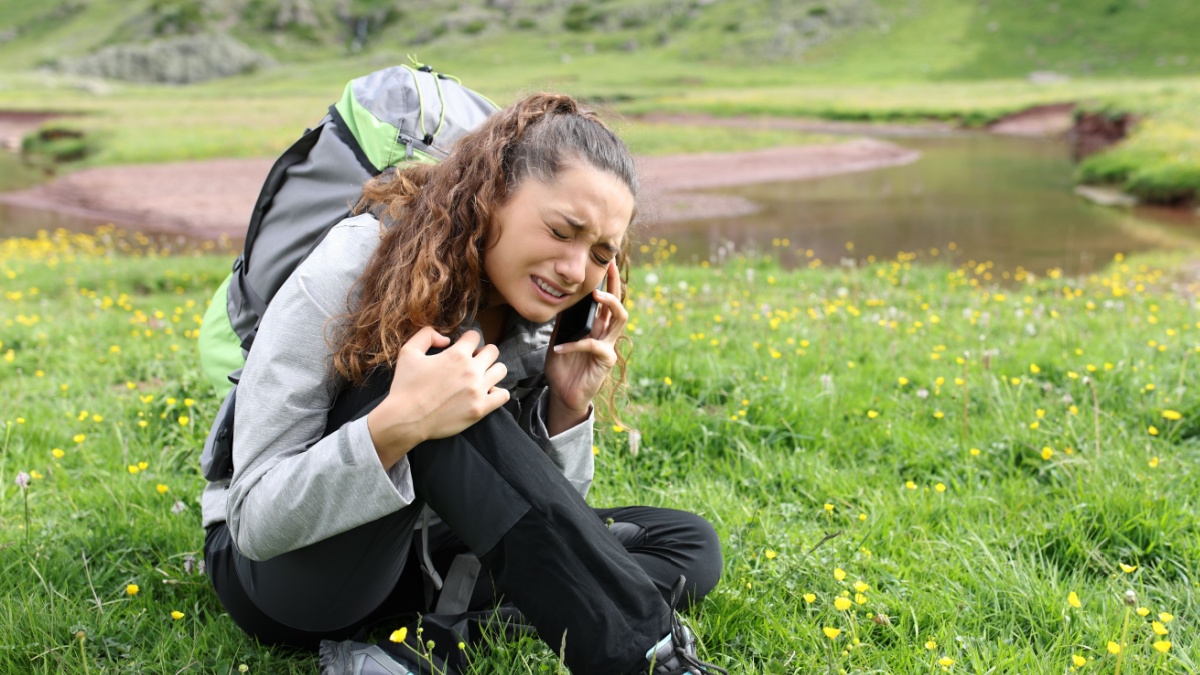 Injured hiker complaining on the grass asking for help on phone.