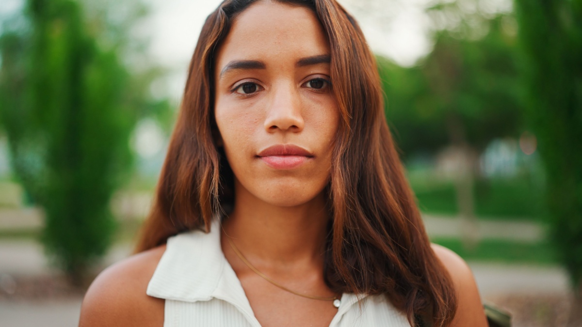 beautiful girl with brown long hair, tanned skin wearing white top raises her head and looks straight into the camera.