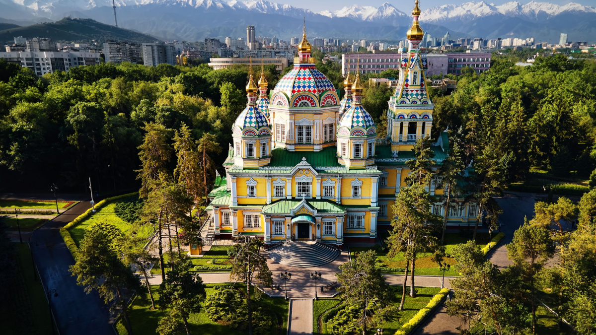 Aerial drone panorama of the Ascension Cathedral Russian Orthodox church and snow mountains at background in Panfilov Park against blue sky in Almaty city, Kazakhstan