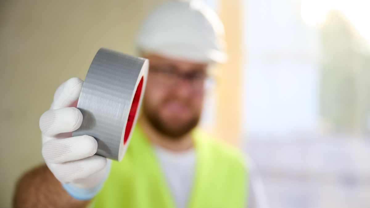 Construction worker in white gloves and a helmet holds a gray reinforced tape. Close up view of grey duct tape. Repair concept.