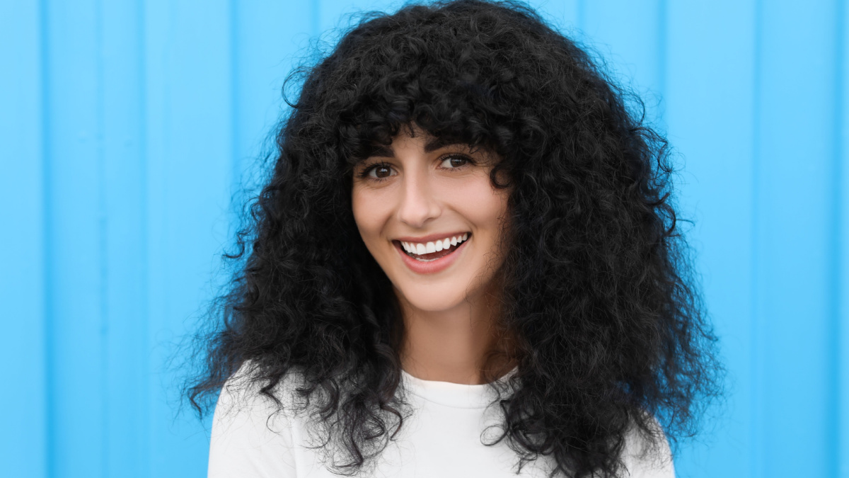 Portrait of beautiful woman posing near light blue wall. Attractive lady smiling and looking into camera.