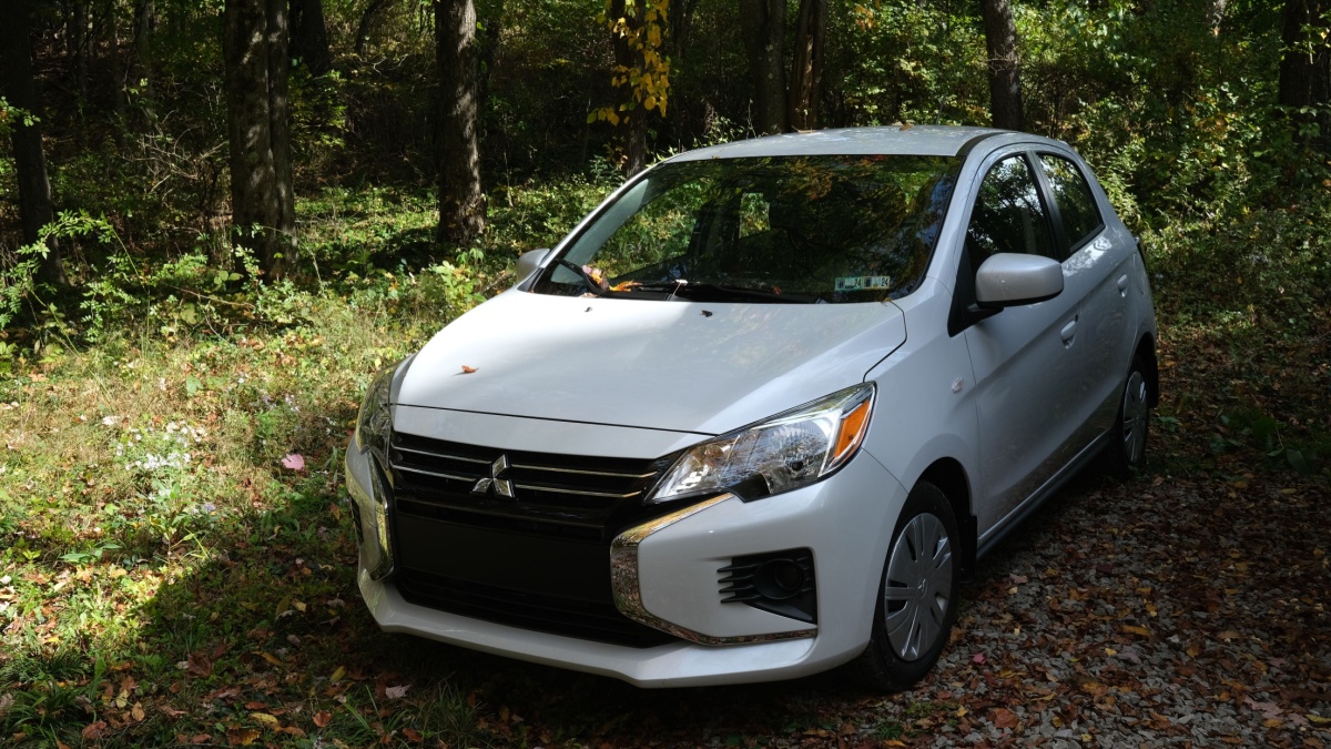 Parked Mitsubishi 2024 Mirage model car seen in a wooded area on a crisp sunny autumn day with fallen leaves surrounding the car.
