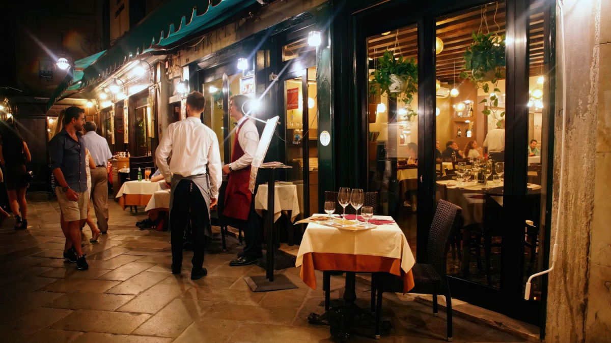 15 Frugal Behaviors That Are Perfectly Fine (No-You're Not Cheap) 7 Nighttime diners at a restaurant in Venice, Italy