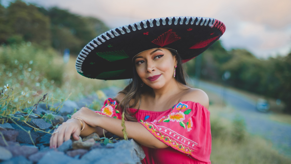 Mexican woman wearing traditional hat and dress. Outdoor portrait next to stone wall.