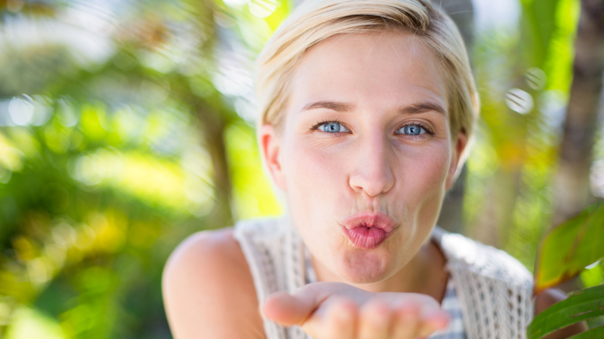 Pretty blonde woman smiling at the camera and blowing kiss in the park.