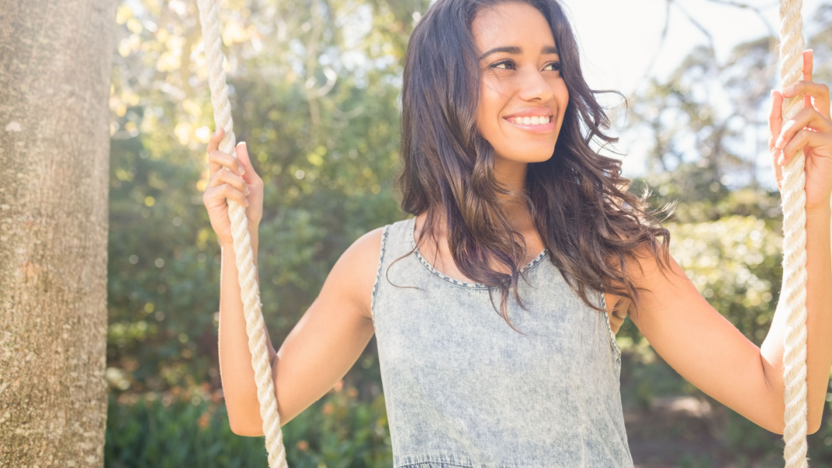 Pretty brunette swinging in park on a sunny day.