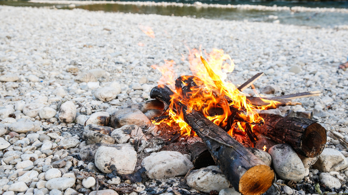 Self-made campfire by the mountain river, lit for cooking, roasting and water purification. Safety and survival, fun family activity concept.