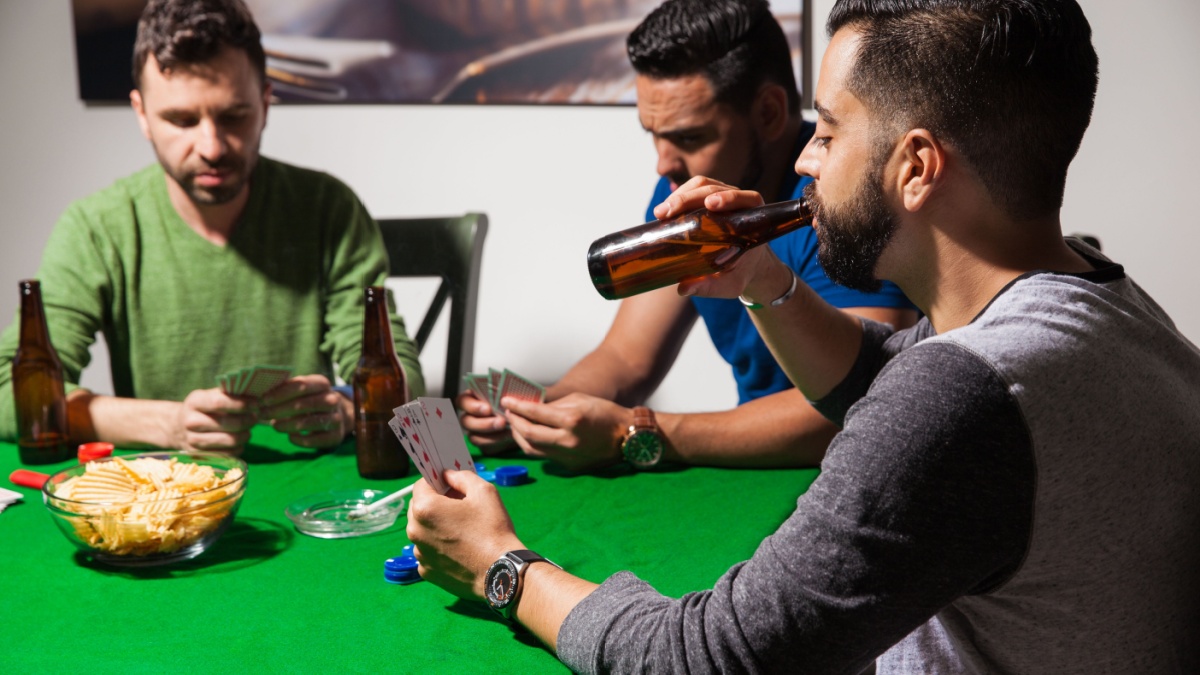 Group of friends playing cards and hanging out at home while enjoying some beer and snacks.