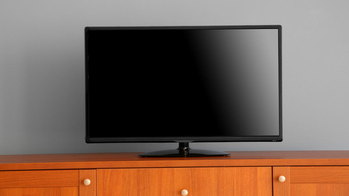 wide screen TV on wooden commode near grey wall