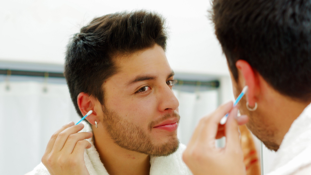 Handsome young man wearing black singlet top looking in mirror, using q-tip during morning routine concept