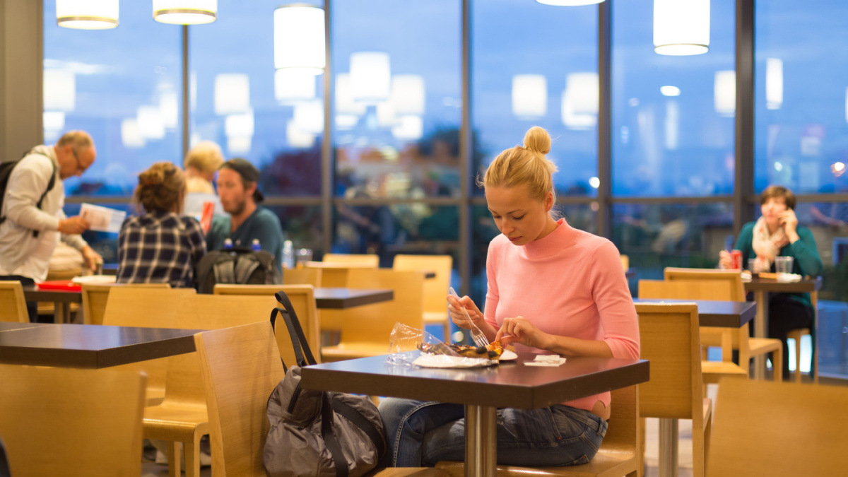 Young female traveler eating pizza at airport restaurant while waiting for late night flight departure.