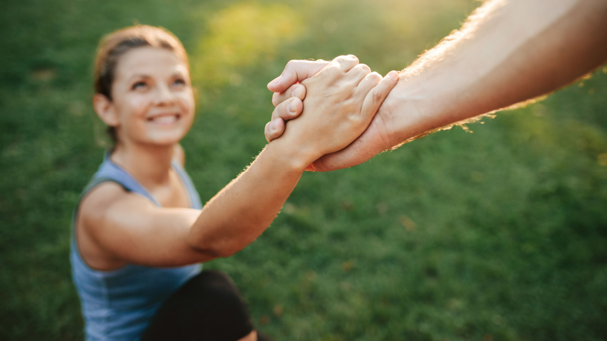 Close up shot of man helping woman to stand up. Focus on hands of couple exercising at park.