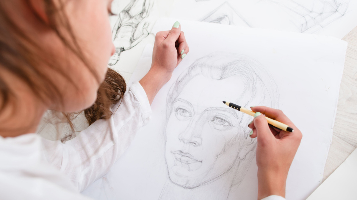 Artist drawing pencil portrait close-up. Woman painter creating picture of woman on big whatman. Art, talent, craft, hobby, occupation concept