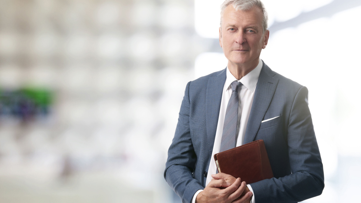 Shot of an elderly managing director with diary standing in conference room after business meeting.
