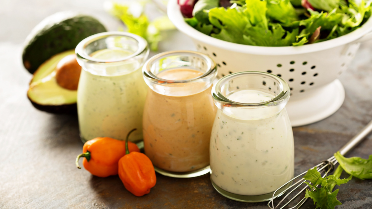 10 Things To Stop Buying and Start Making Yourself 6 Homemade ranch dressing variety in small jars with herbs, avocado and hot pepper