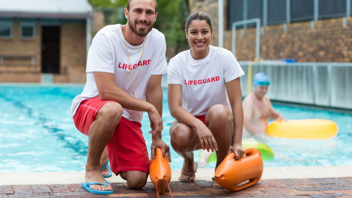 Portrait of male and female lifeguards holding rescue cans at poolside