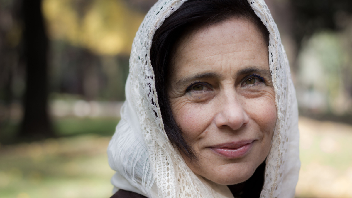 Portrait of mature lady covering her head with hijab style white shawl in the park. Young looking woman with white veil over head, Muslim look. Female model with charming serene look and soft skin.