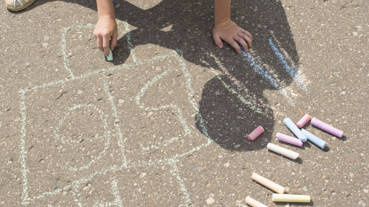 Child playing outside and drawing on the asphalt.