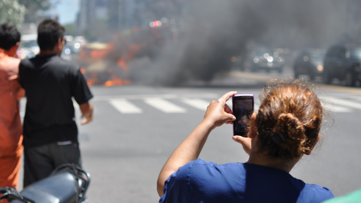 woman using a cell phone to film a burning car downtown buenos aires, argentina. Focus is on cell phone and hand of the woman.