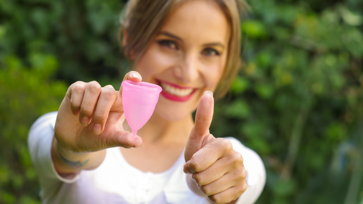 Close up of a young woman pointing in front of her a menstrual cup in one hand, Gynecology concept, ith her thums up aproving the use of the mentrual cup