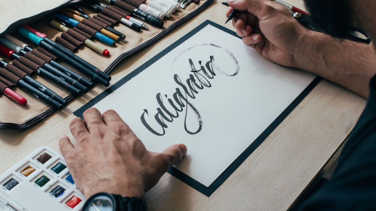 View on big sheet of white paper canvas with word calligraphy spelled on top using brush with black ink by font designer or creative artist freelancer working on project in home studio