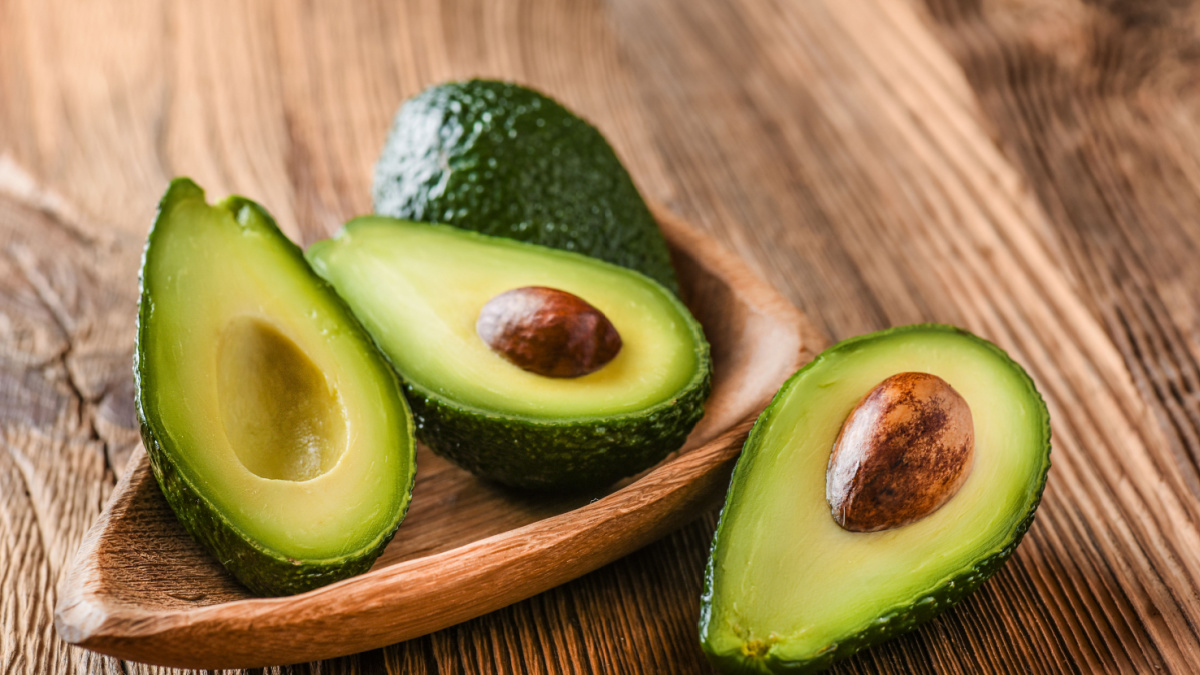 Avocado on old wooden table.Halfs on wooden bowl.