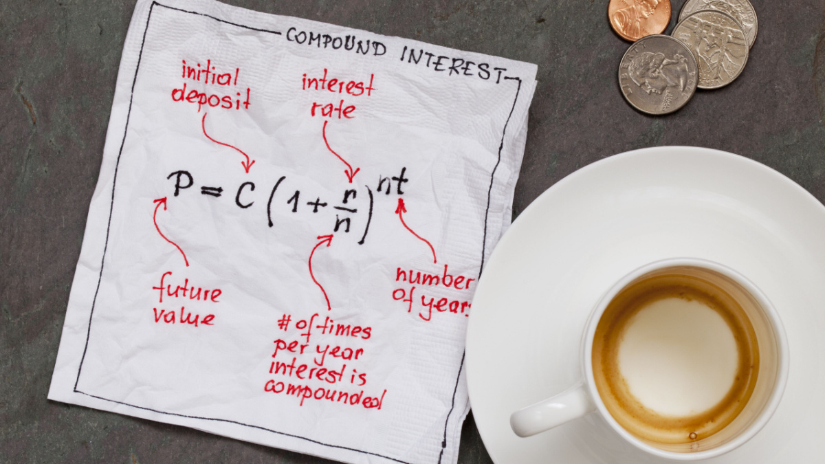 compound interest equation on a cocktail napkin with empty coffee cup and coins on a slate stone table