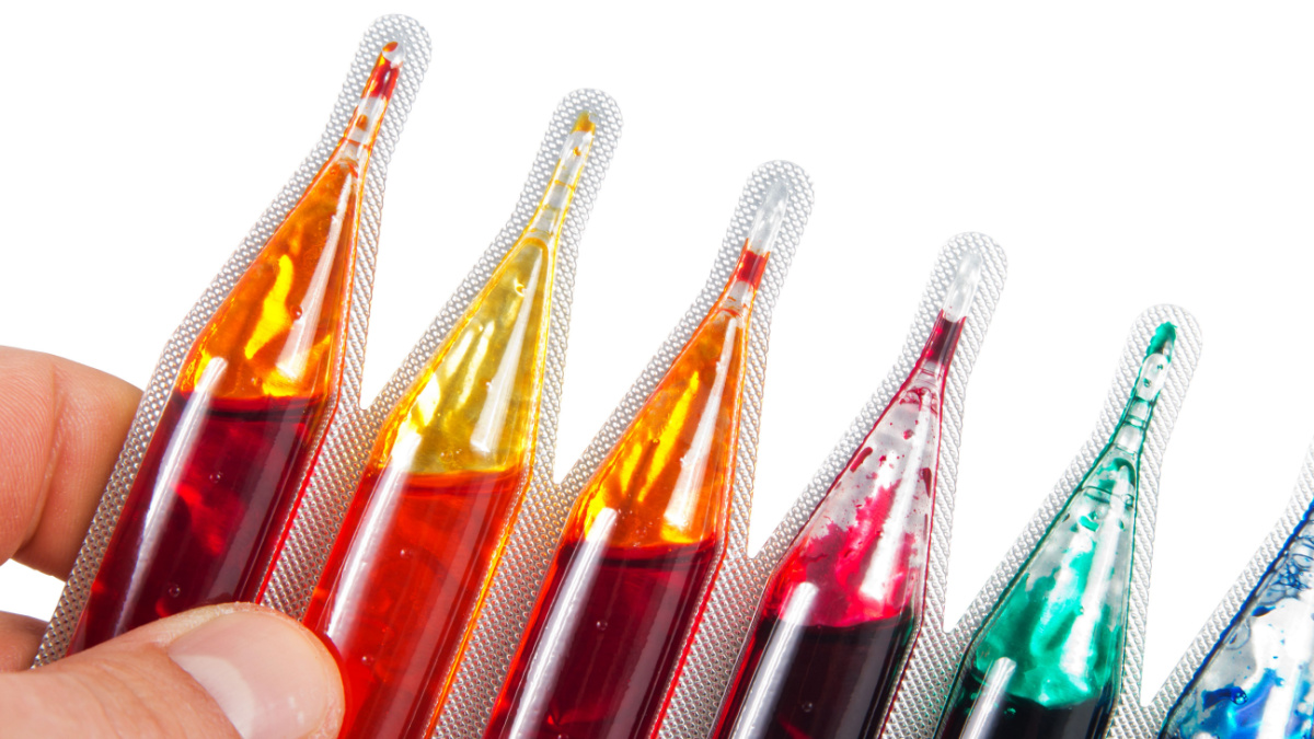 Detail of a hand holding food dye in different colors over a white background