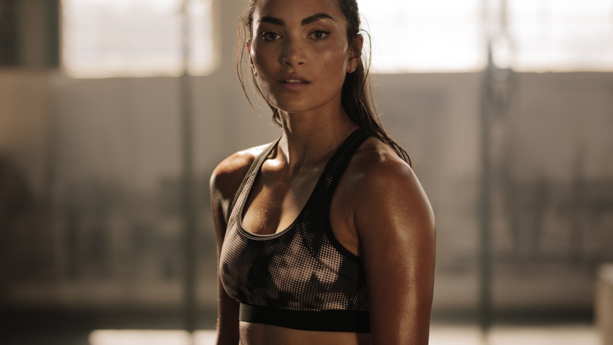 Strong and determined female in sportswear standing in the gym and looking at camera. Sportswoman after intense crossing training workout session in gym.