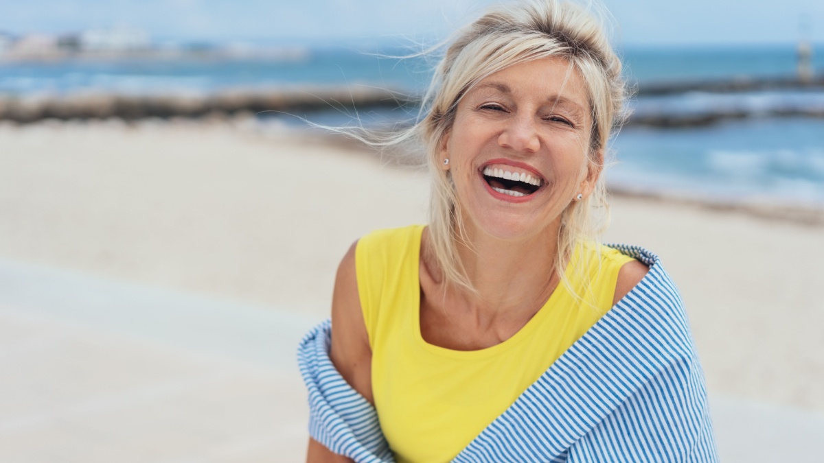 Laughing vivacious blond woman with a sense of humour standing on a tropical beach.