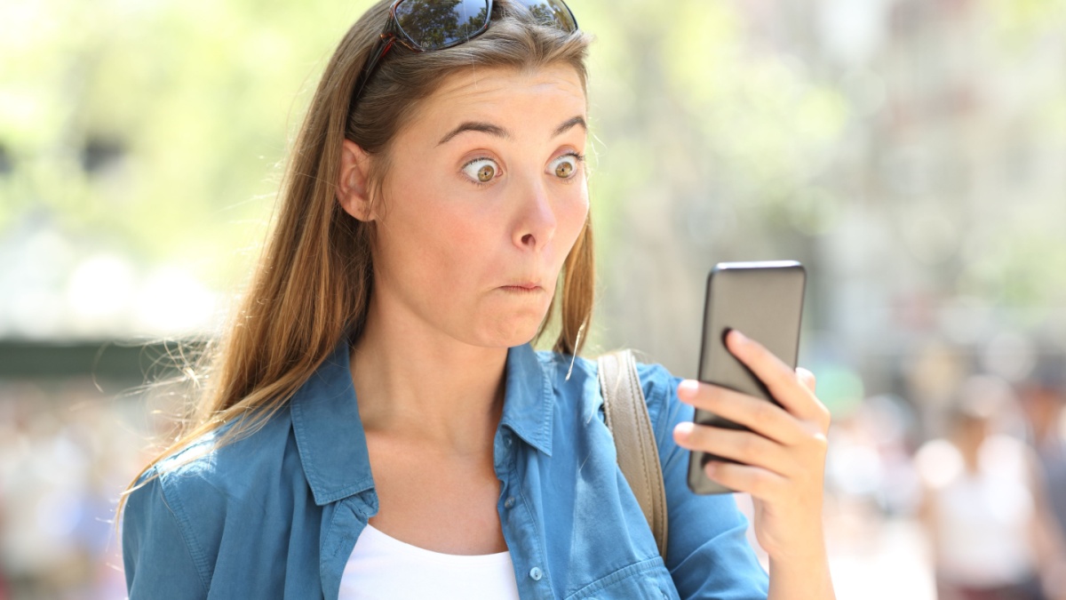 Portrait of an astonished woman reading smart phone content in the street.