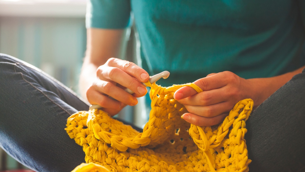 Woman knits crochet. The girl sits on the couch and knits from knitting yarn. Crochet thick threads. Home comfort.