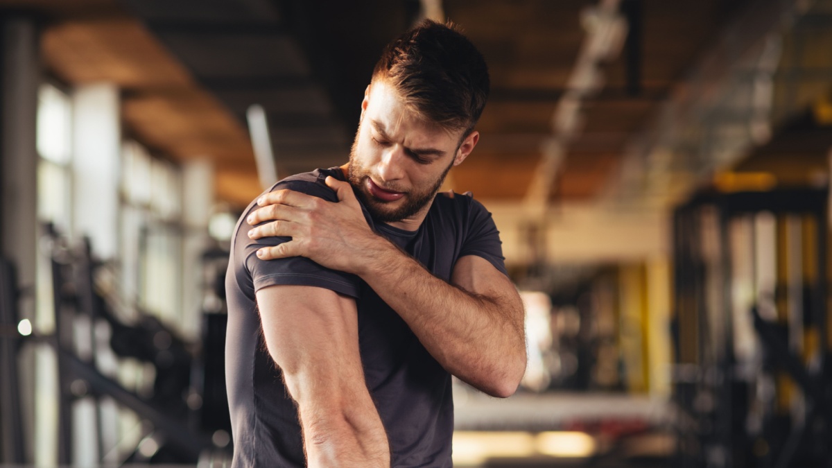 Handsome young man feeling the pain in shoulder at the gym